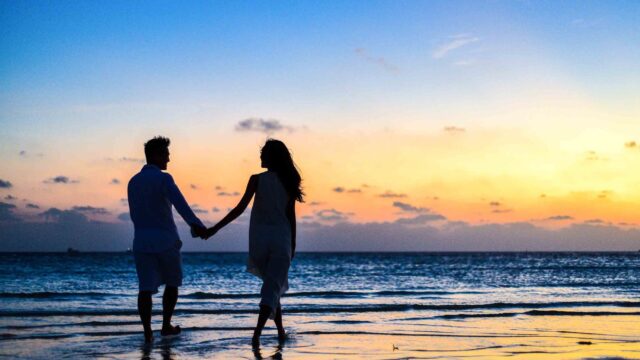 man and woman holding hands walking on seashore during sunrise